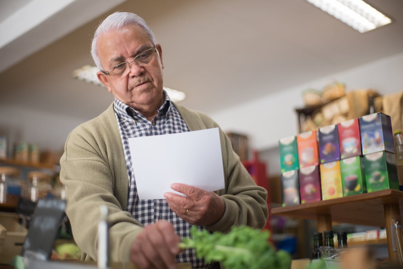 Elderly man shopping in a Portuguese grocery store, holding a paper list.